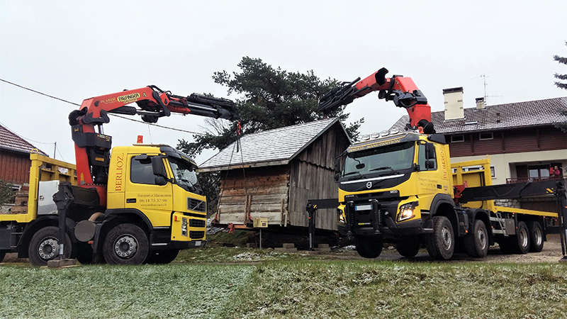 Levage d'un chalet à deux camions équipés de bras de grue